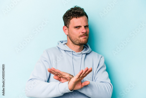 Obraz na plátne Young caucasian man isolated on blue background doing a denial gesture