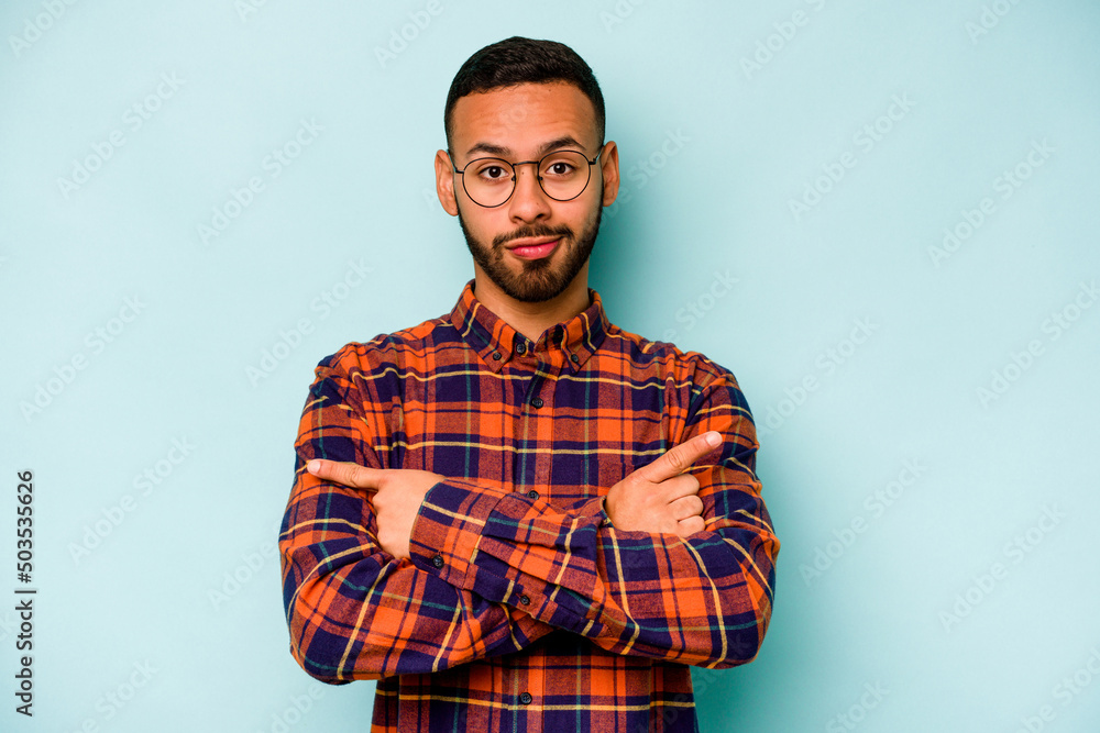 Young hispanic man isolated on blue background points sideways, is trying to choose between two options. Young hispanic man isolated on blue background points sideways, is trying to choose between two options.