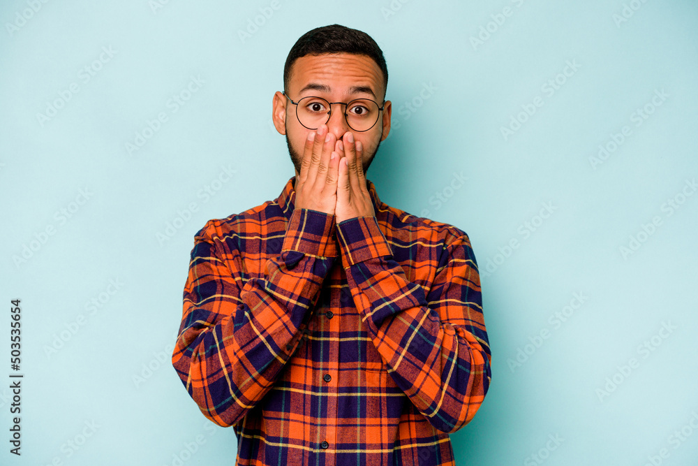 Young hispanic man isolated on blue background shocked, covering mouth with hands, anxious to discover something new.
