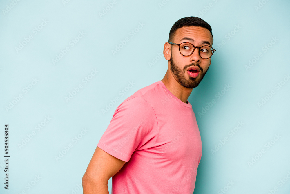 Young hispanic man isolated on blue background looks aside smiling, cheerful and pleasant. Young hispanic man isolated on blue background looks aside smiling, cheerful and pleasant.