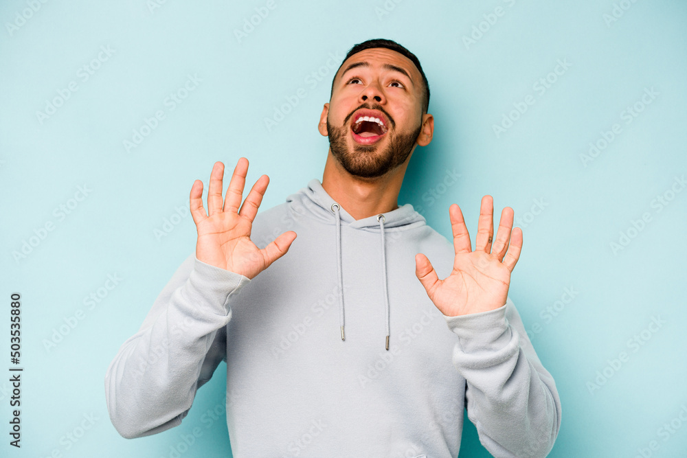 Young hispanic man isolated on blue background screaming to the sky, looking up, frustrated. Young hispanic man isolated on blue background screaming to the sky, looking up, frustrated.