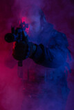 soldier in full gear with weapons. a man in headphones, body armor, with a backpack and a belt. red background. colored, blue-red light. smoke around the military. chemical attack. protection concept