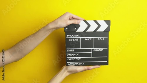 Hand holding movie clapperboard on yellow background