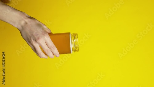 Female hands holding jar of honey with stick honey spoon on yellow background