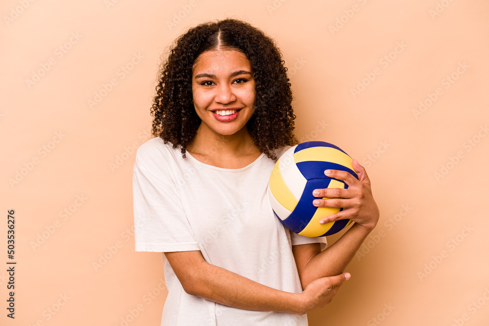 Young African American woman playing volleyball isolated on beige background laughing and having fun.