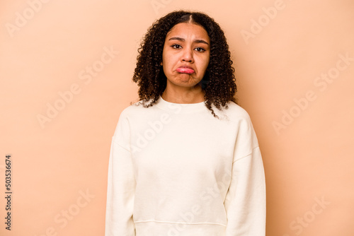 Young African American woman isolated on beige background sad, serious face, feeling miserable and displeased. © Asier