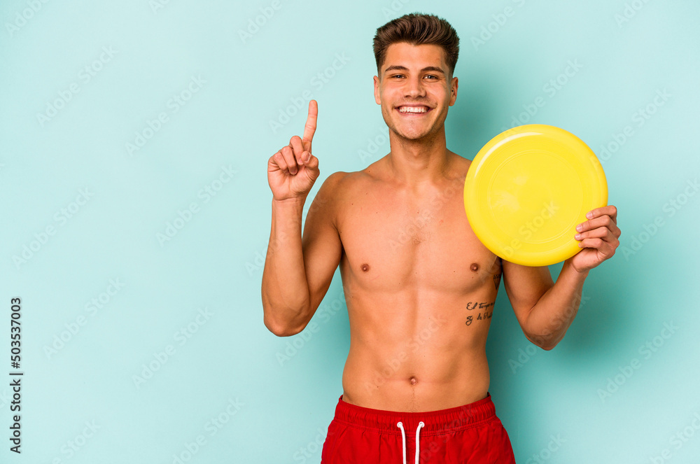 Young caucasian man playing with frisky isolated on blue background showing number one with finger.
