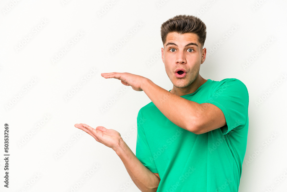 Young caucasian man isolated on white background shocked and amazed holding a copy space between hands. Young caucasian man isolated on white background shocked and amazed holding a copy space between hands.