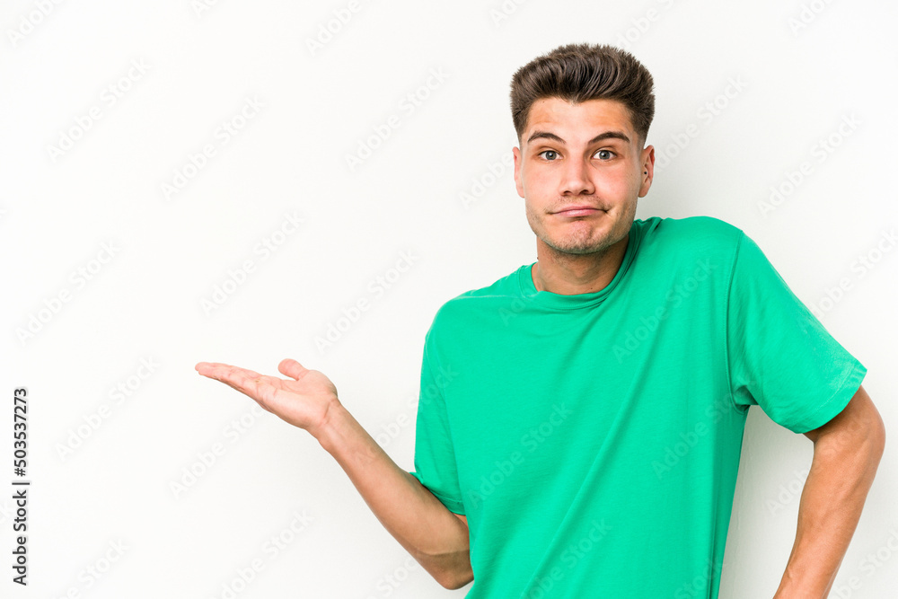 Young caucasian man isolated on white background showing a copy space on a palm and holding another hand on waist. Young caucasian man isolated on white background showing a copy space on a palm and holding another hand on waist.