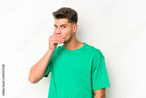 Young caucasian man isolated on white background covering mouth with hands looking worried.