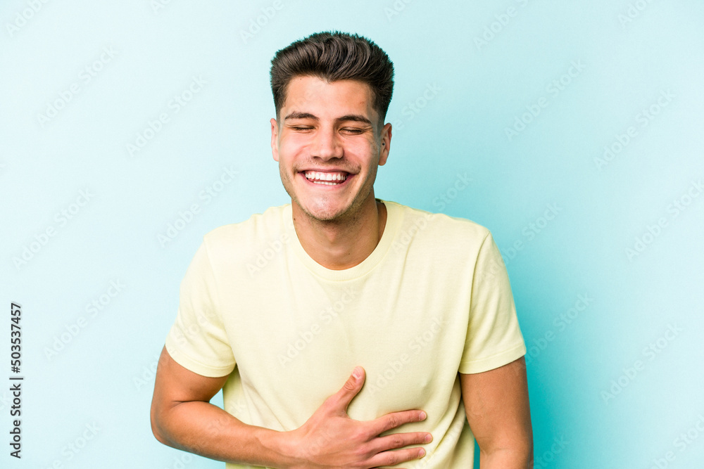 Young caucasian man isolated on blue background touches tummy, smiles gently, eating and satisfaction concept. Young caucasian man isolated on blue background touches tummy, smiles gently, eating and satisfaction concept.