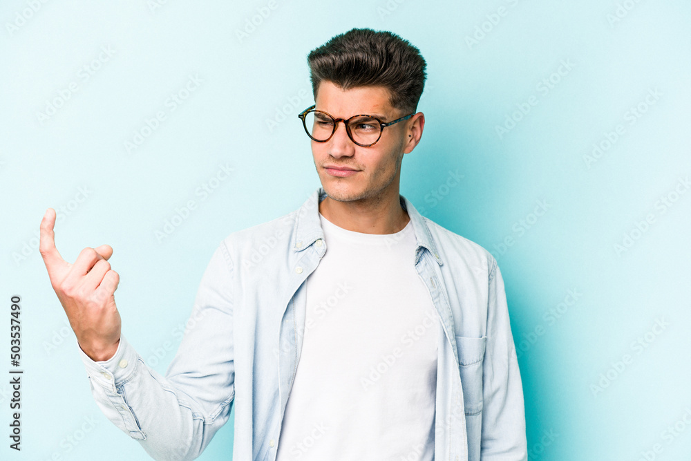 Young caucasian man isolated on blue background pointing with finger at you as if inviting come closer. Young caucasian man isolated on blue background pointing with finger at you as if inviting come closer.