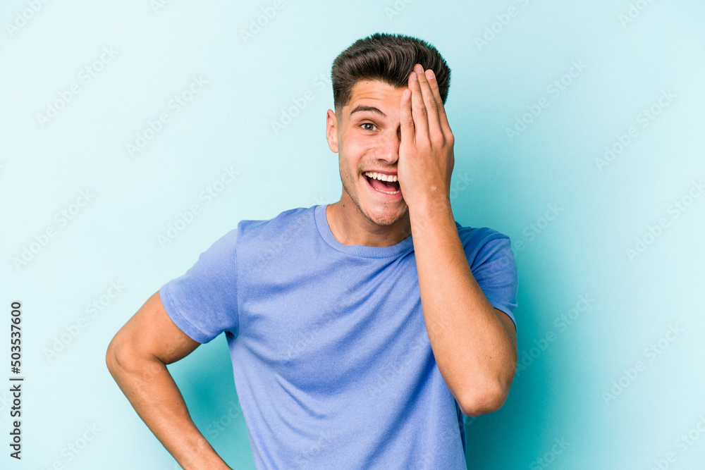Young caucasian man isolated on blue background having fun covering half of face with palm. Young caucasian man isolated on blue background having fun covering half of face with palm.