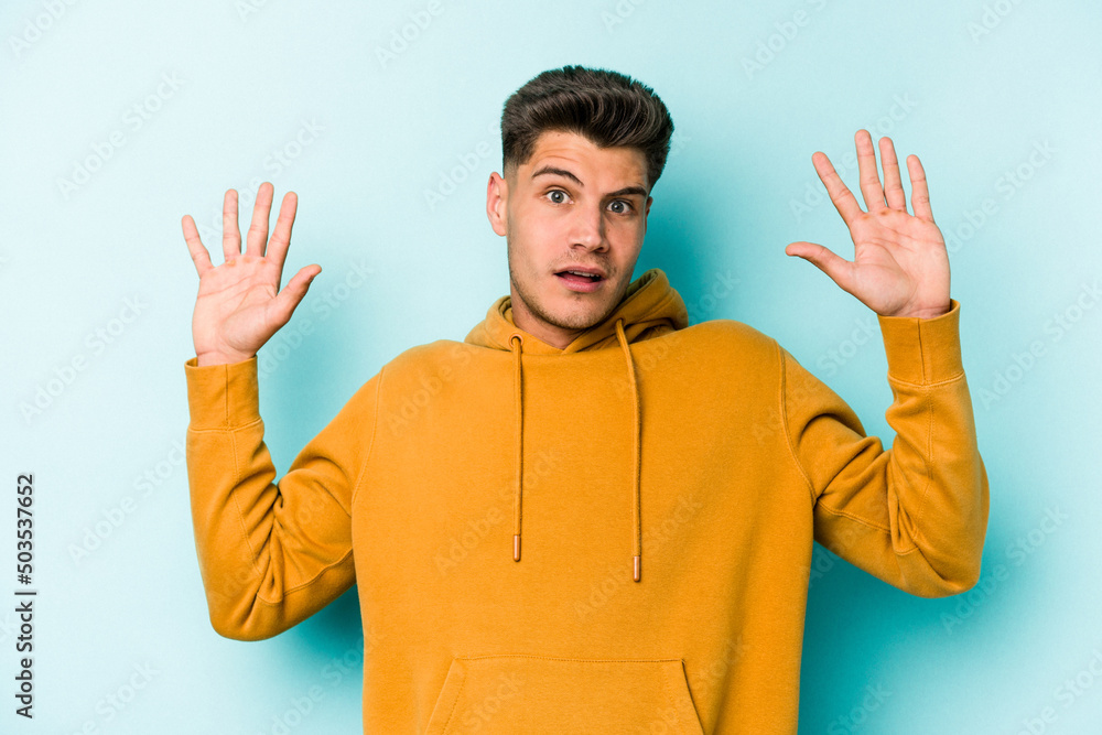 Young caucasian man isolated on blue background being shocked due to an imminent danger Young caucasian man isolated on blue background being shocked due to an imminent danger