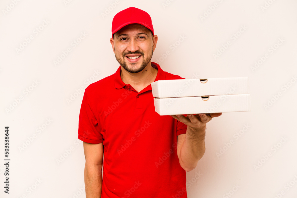 Young delivery man holding pizzas isolated on beige background laughing and having fun. Young delivery man holding pizzas isolated on beige background laughing and having fun.