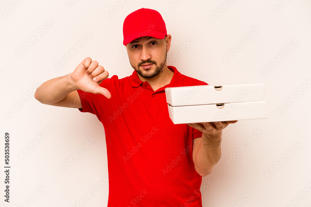 Young delivery man holding pizzas isolated on beige background showing a dislike gesture, thumbs down. Disagreement concept. Young delivery man holding pizzas isolated on beige background showing a dislike gesture, thumbs down. Disagreement concept.