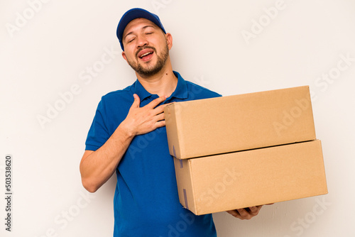 Hispanic delivery man isolated on white background laughs out loudly keeping hand on chest. © Asier