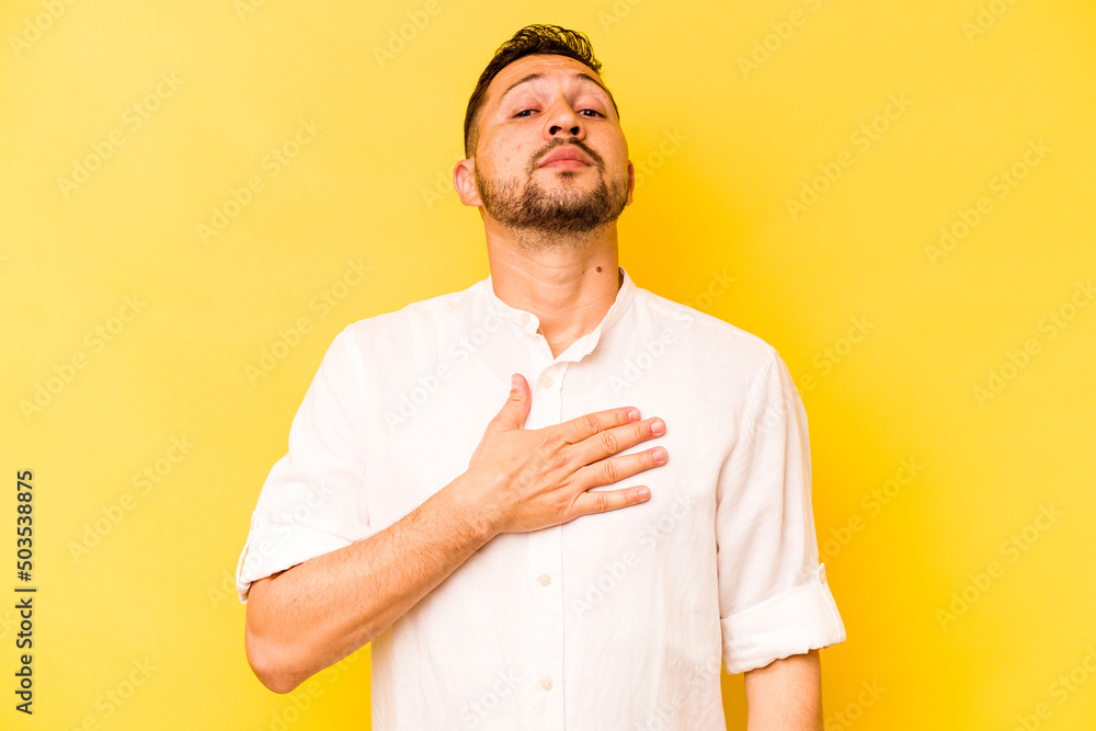 Young hispanic man isolated on yellow background taking an oath, putting hand on chest. Young hispanic man isolated on yellow background taking an oath, putting hand on chest.