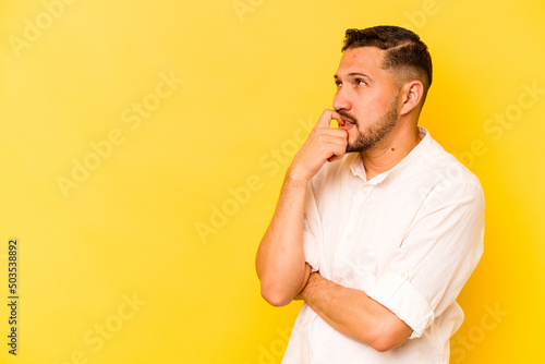 Young hispanic man isolated on yellow background relaxed thinking about something looking at a copy space.