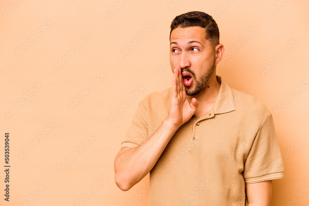 Young hispanic man isolated on beige background is saying a secret hot braking news and looking aside Young hispanic man isolated on beige background is saying a secret hot braking news and looking aside