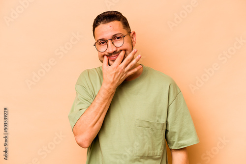 Young hispanic man isolated on beige background doubting between two options. © Asier