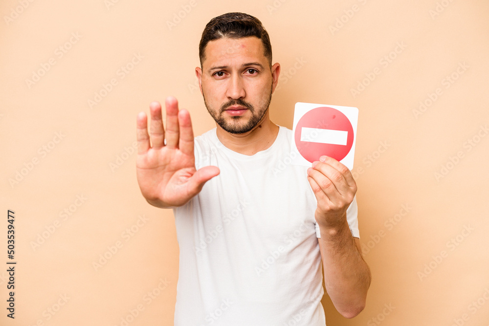 Hispanic caucasian man holding a forbidden sign isolated on beige background Hispanic caucasian man holding a forbidden sign isolated on beige background