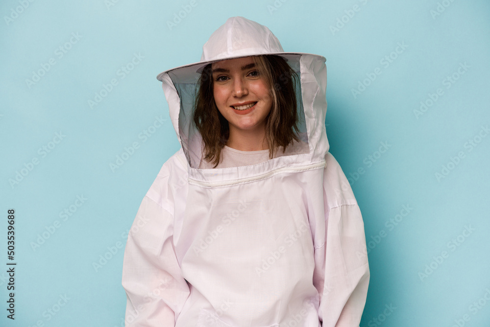 Young caucasian beekeeper woman isolated on blue background happy, smiling and cheerful. Young caucasian beekeeper woman isolated on blue background happy, smiling and cheerful.
