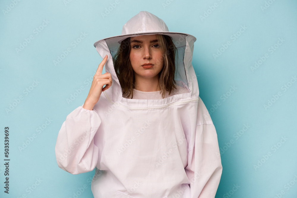 Young caucasian beekeeper woman isolated on blue background pointing temple with finger, thinking, focused on a task. Young caucasian beekeeper woman isolated on blue background pointing temple with finger, thinking, focused on a task.