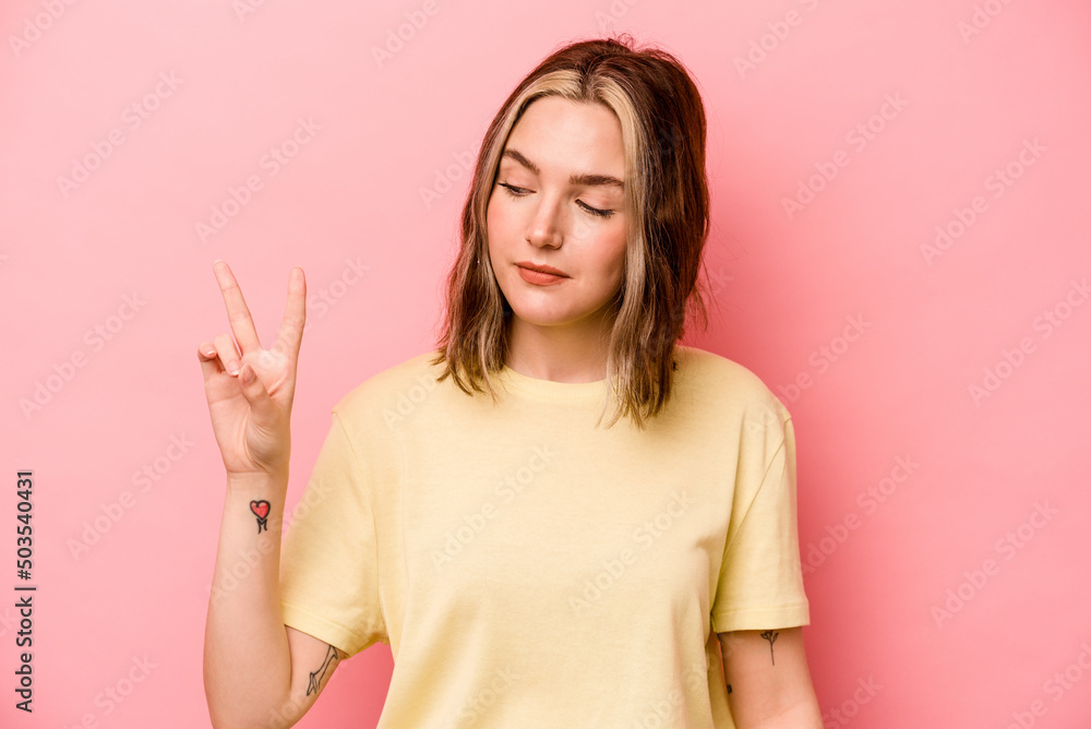 Young caucasian woman isolated on pink background joyful and carefree showing a peace symbol with fingers. Young caucasian woman isolated on pink background joyful and carefree showing a peace symbol with fingers.