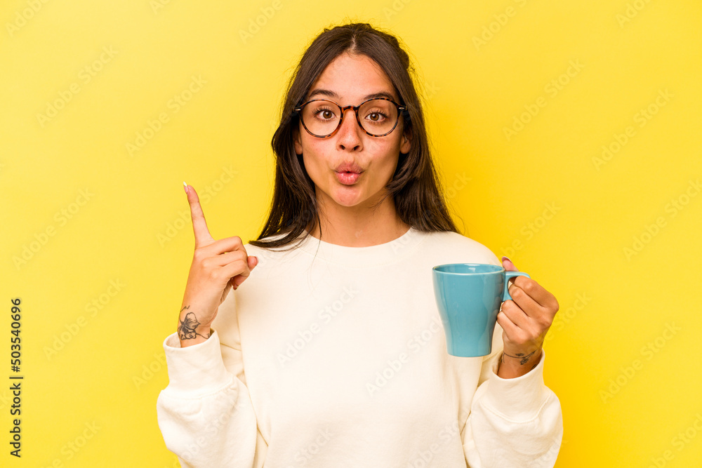 Young hispanic woman holding a mug isolated on yellow background having some great idea, concept of creativity. Young hispanic woman holding a mug isolated on yellow background having some great idea, concept of creativity.