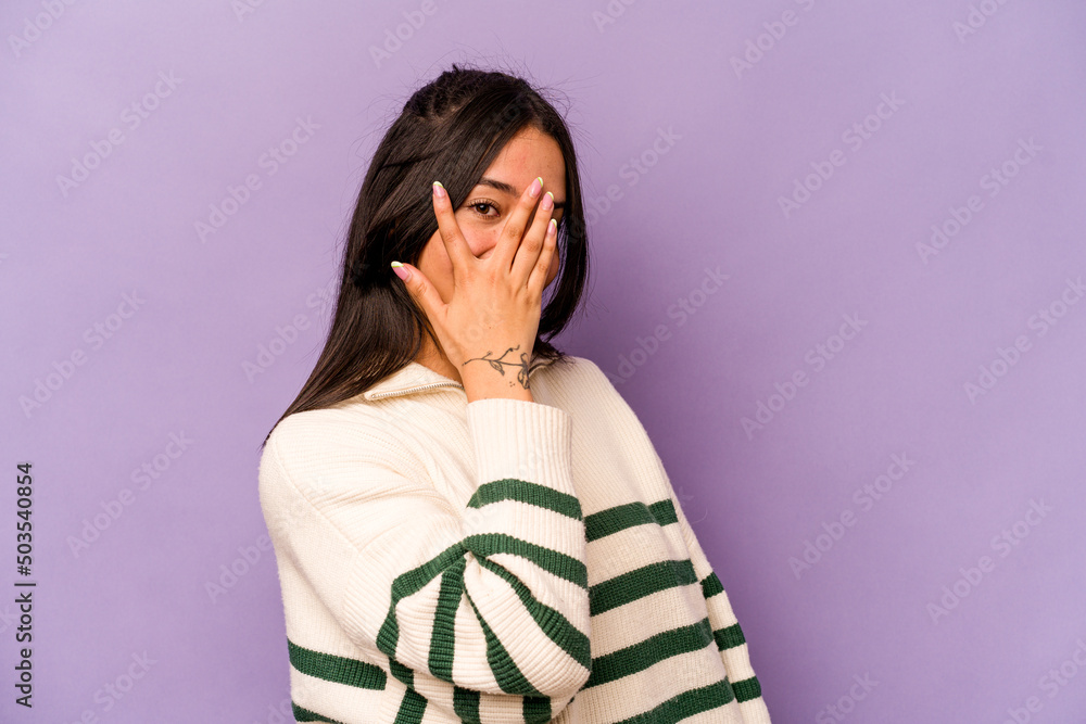 Young hispanic woman isolated on purple background blink at the camera through fingers, embarrassed covering face. Young hispanic woman isolated on purple background blink at the camera through fingers, embarrassed covering face.