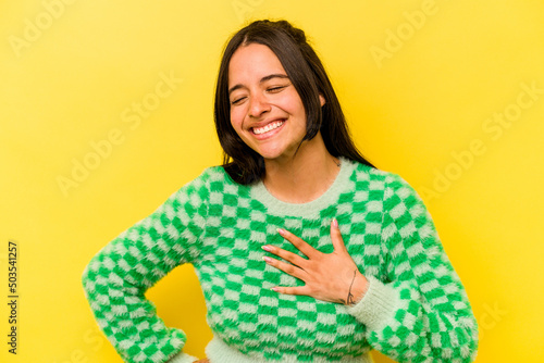 Young hispanic woman isolated on yellow background laughing keeping hands on heart, concept of happiness. © Asier