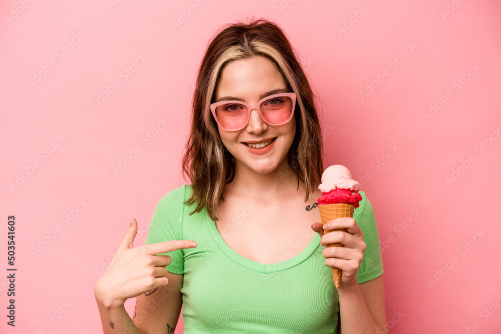Young caucasian woman holding an ice cream isolated on pink background person pointing by hand to a shirt copy space, proud and confident Young caucasian woman holding an ice cream isolated on pink background person pointing by hand to a shirt copy space, proud and confident