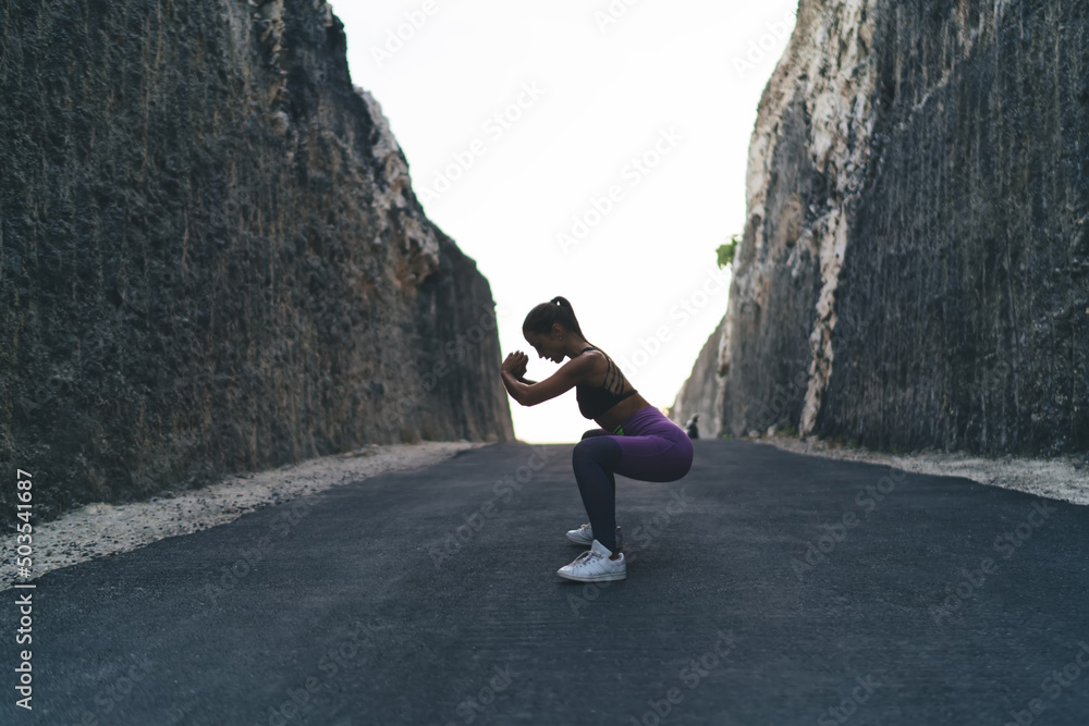 Female in sportswear doing squats during morning workout - determined on results and slimming, active Caucasian woman concentrated on exercises keeping healthy lifestyle and vitality wellness