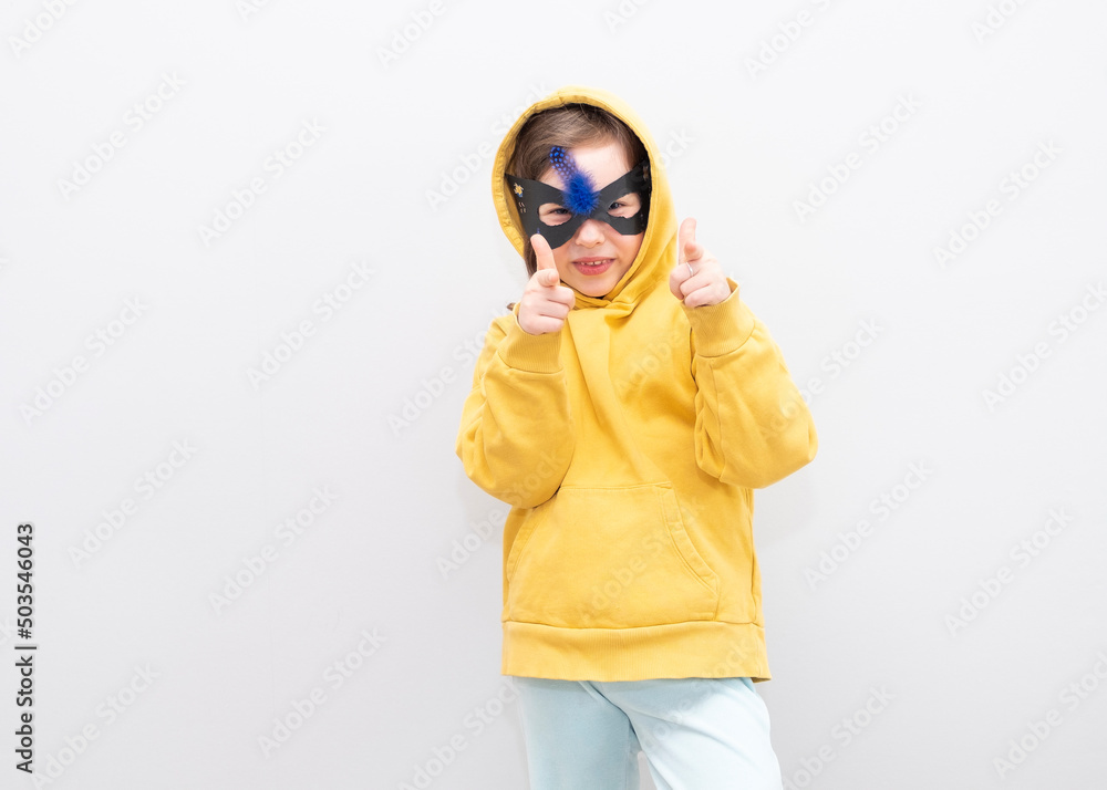 Girl 6 years old in a black mask, emotionally shows the direction with her fingers. Gray background and copy space.