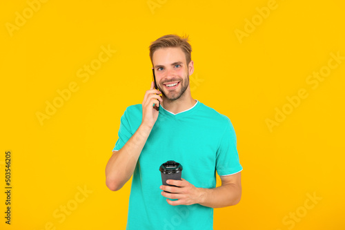 happy guy with coffee speak on phone on yellow background, conversation