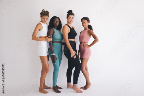 Group Of Body Positive Females with Different Figure Types in Sportswear near white copy space in gym studio, four multicultural Women in tracksuit enjoying own Beauty keeping healthy lifestyle