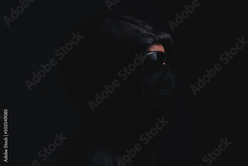 Stylish man in dark hoodie with black glasses and mask dark background, hacker, attacker and bandit.