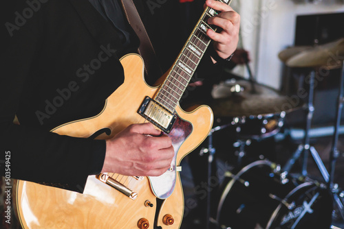 Concert view of an electric guitar player with vocalist and musical jazz band orchestra performing in the background, guitarist on the stage