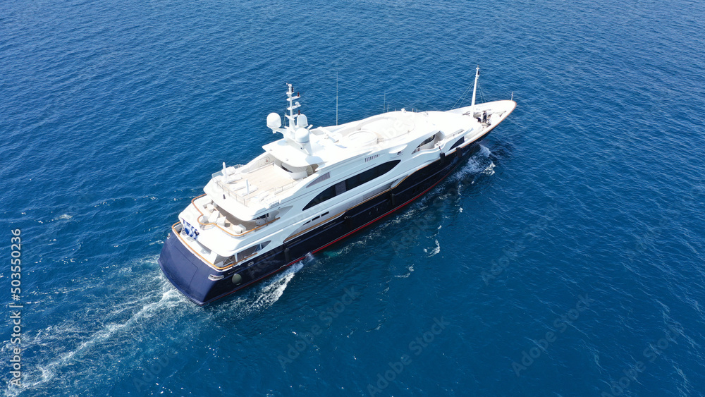 Aerial drone top down photo of luxury yacht with wooden deck cruising in deep blue sea of Mykonos island, Cyclades, Greece