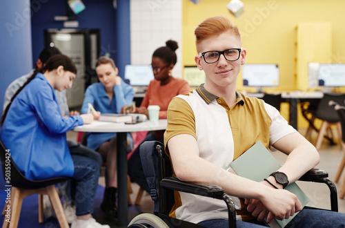 Vibrant portrait of red haired young man with disability in college library looking at camera, copy space