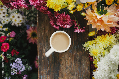 Good fall morning. Warm cup of coffee and beautiful autumn flowers on rustic wooden background flat lay. Stylish mug with cappuccino among colorful asters and dahlias composition.