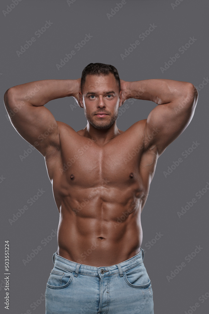Shot of bodybuilder with naked torso dressed in denim pants holding his head looking at camera. Shot of bodybuilder with naked torso dressed in denim pants holding his head looking at camera.