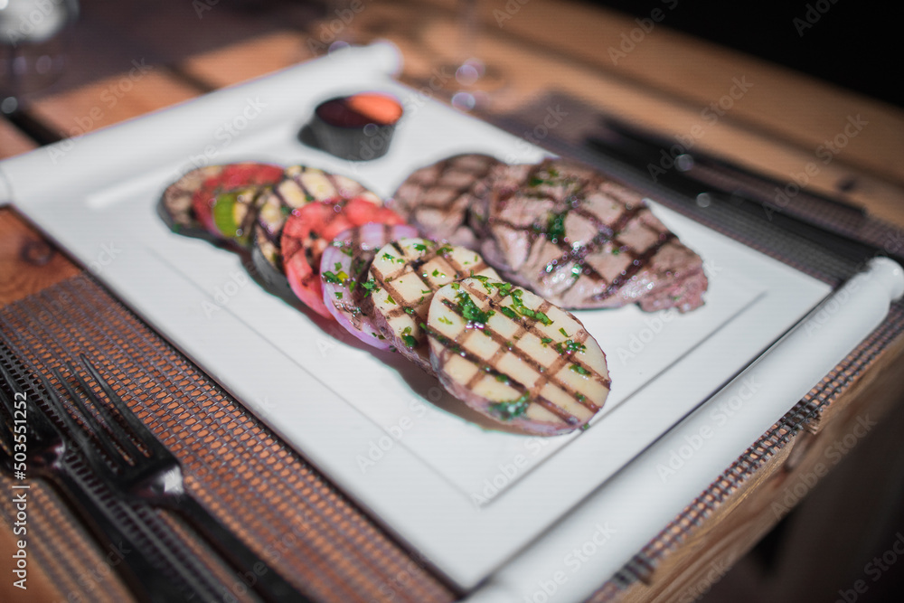 A plate of grilled beef meat with grilled slices of potatoes, tomatoes and onions A plate of grilled beef meat with grilled slices of potatoes, tomatoes and onions
