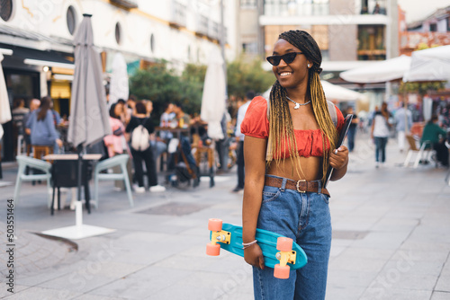 Young African woman in the city with her skateboard and her laptop, lifestyle concept