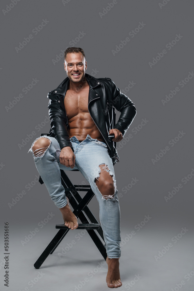 Shot of smiling man bodybuilder dressed in stylish clothes sitting on chair.