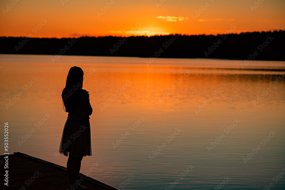 A lady's silhouette against the background of a calm sunset beach