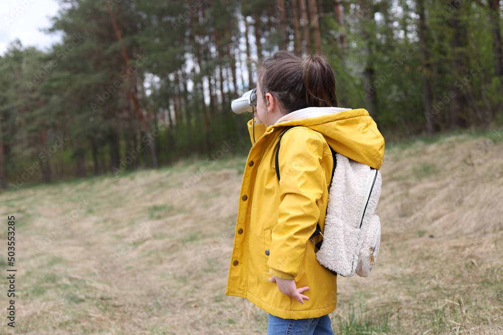 Little explorer, girl with binoculars plays in the forest. Search and research. Travel and adventure concept. Kids club, camping