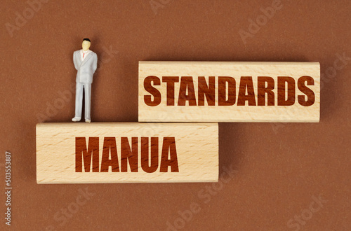 On wooden blocks with the inscription - Standards Manua, there is a miniature figure of a businessman. photo