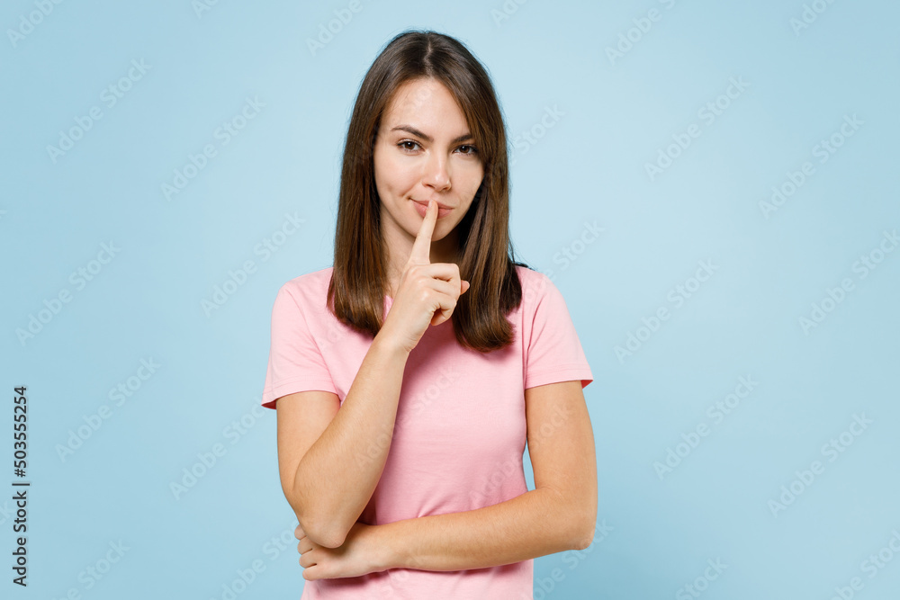 Young secret happy caucasian woman 20s wearing pink t-shirt say hush be quiet with finger on lips shhh gesture isolated on pastel plain light blue background studio portrait. People lifestyle concept. Young secret happy caucasian woman 20s wearing pink t-shirt say hush be quiet with finger on lips shhh gesture isolated on pastel plain light blue background studio portrait. People lifestyle concept.